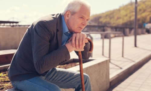 Pleasant white-haired elderly man resting his chin on his hands folded on a cane